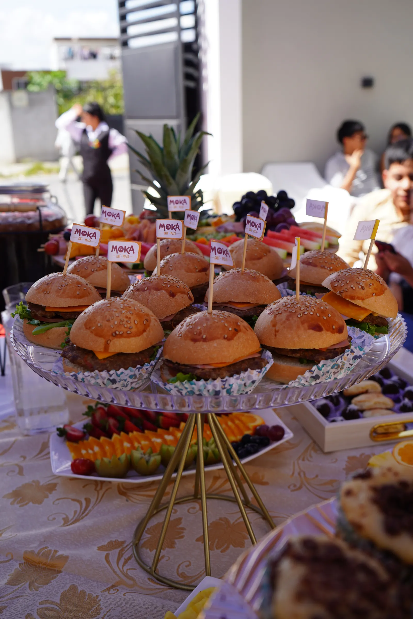 Torre de mini hamburguesas con banderines de Moka Café sobre la mesa del evento